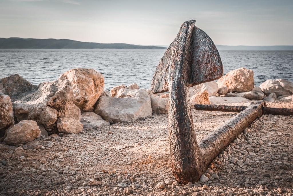 Old rusty anchor on the beach with stones